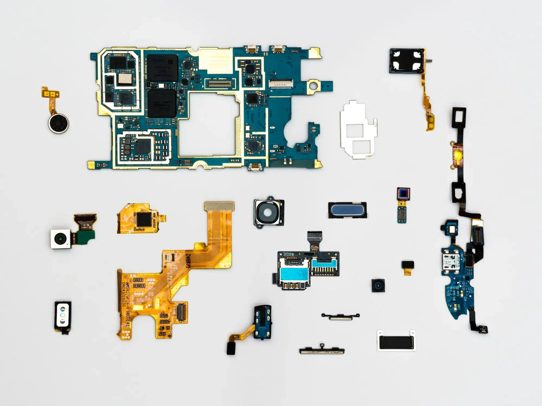 Disassembled smartphone parts flat-lay on white: main logic board in teal, flex ribbons, cameras, sensors, speakers, and connectors in organized spread.