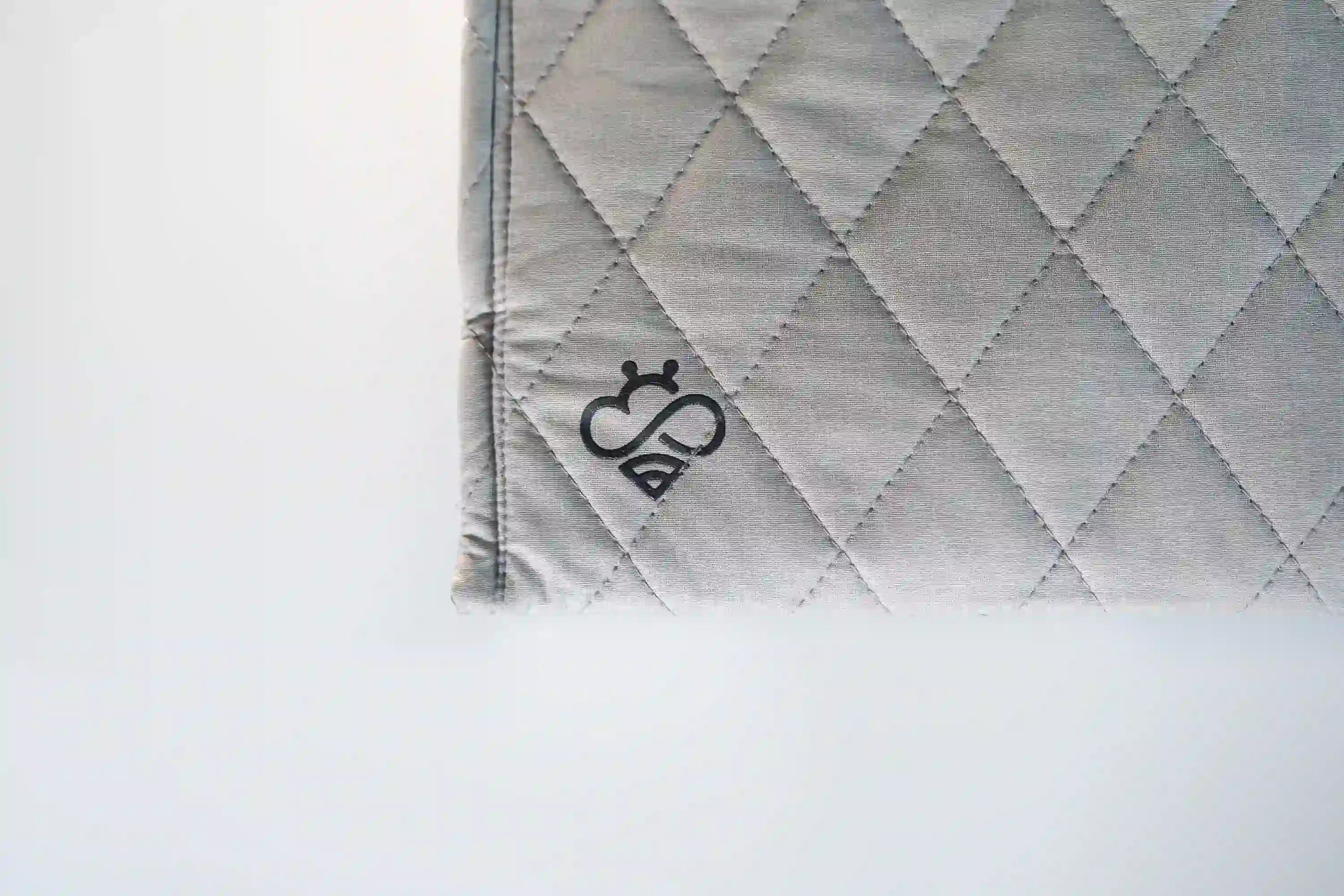 Gray quilted Hapbee Sleep Pad fabric close-up with diamond stitching and embroidered black Hapbee logo.
